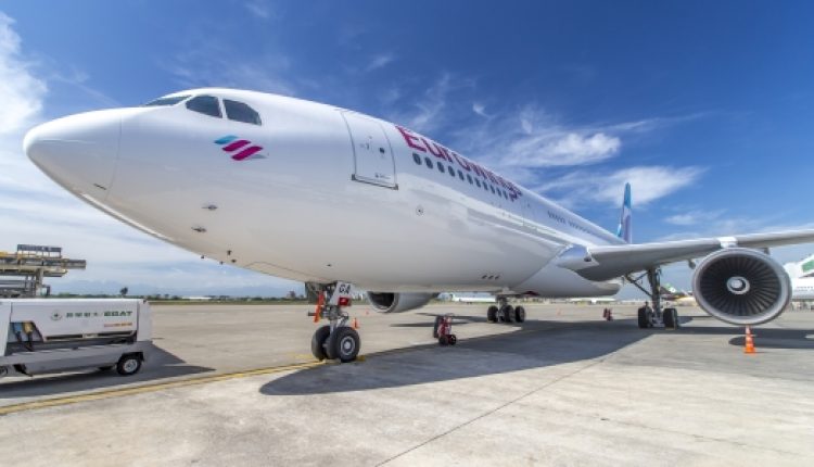 Ein großes weißes Flugzeug einer Fluggesellschaft, das auf dem Rollfeld eines Flughafens unter einem strahlend blauen Himmel geparkt ist.