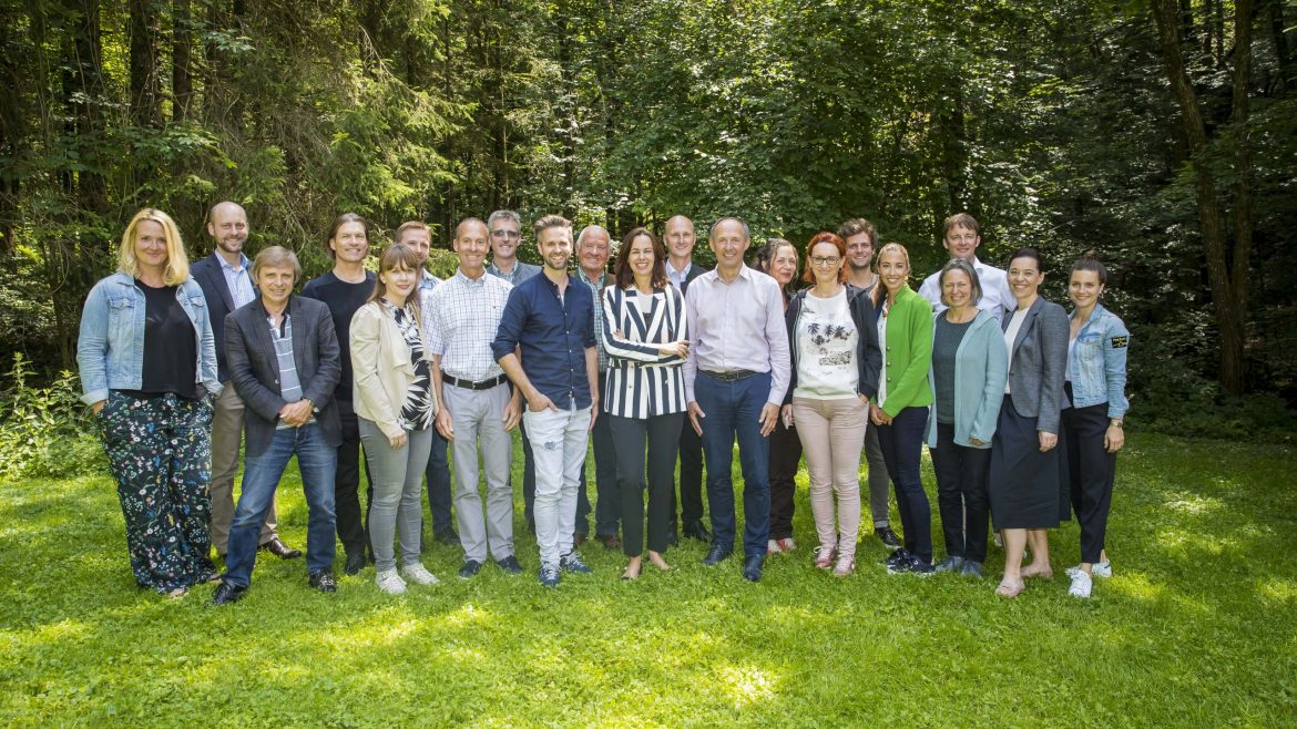 Eine Gruppe von Menschen steht zusammen und lächelt in einem üppigen, grünen Wald.