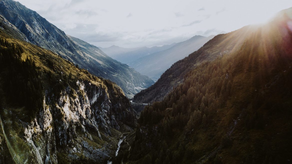 Ein sonnenbeschienenes Gebirgstal, das sich durch bewaldete Hänge schlängelt - perfekt, um neue Reisetrends zu entdecken.