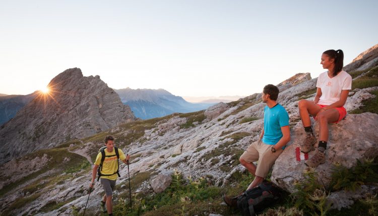 Drei Wanderer genießen Bergsport bei Sonnenaufgang an einem felsigen Berghang und bewundern die atemberaubende Aussicht.