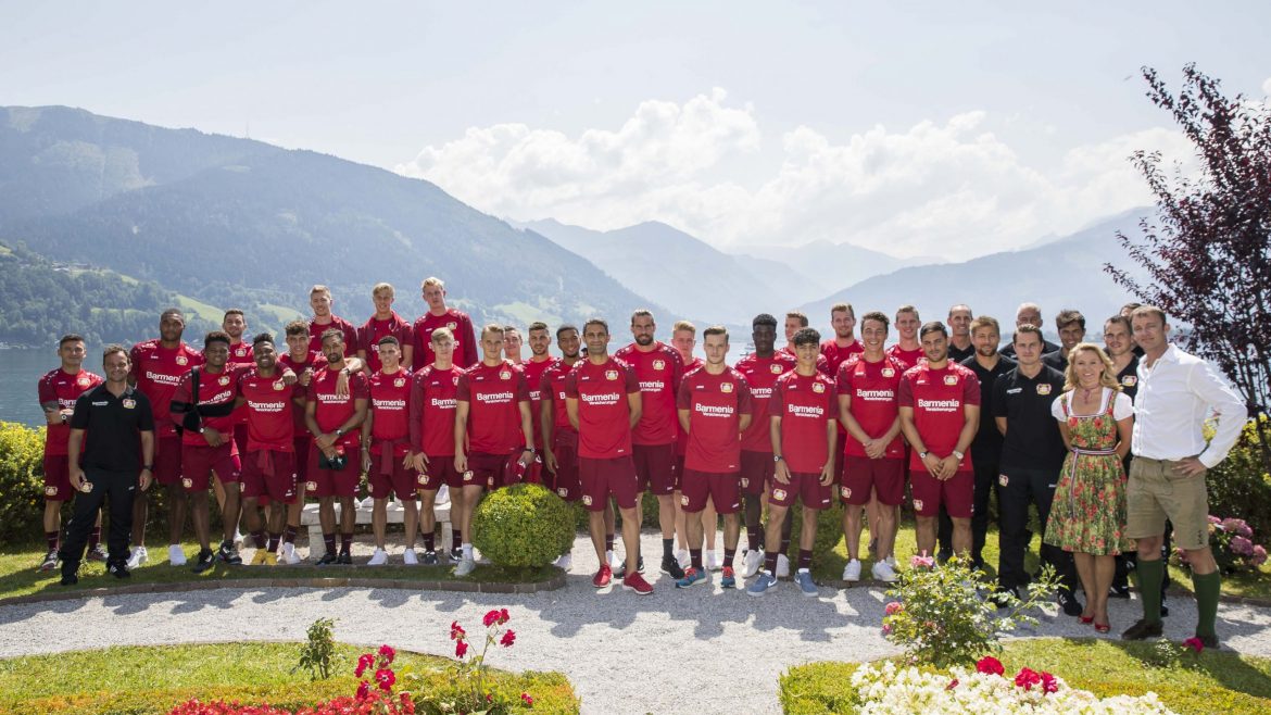 Eine Fußballmannschaft in roten Trikots posiert im Freien in einem Garten mit Bergen im Hintergrund.