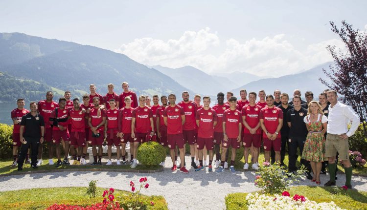 Eine Fußballmannschaft in roten Trikots posiert im Freien in einem Garten mit Bergen im Hintergrund.