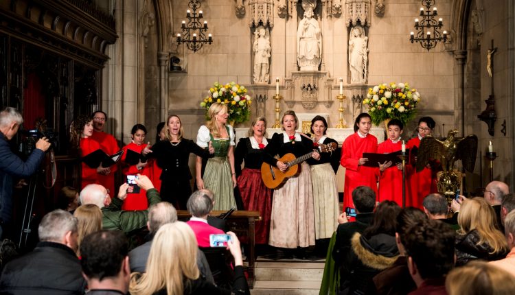 Ein Chor singt in einer Kirche; eine Frau spielt Gitarre, während das Publikum zusieht und Fotos macht.