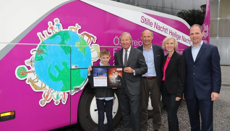 Fünf Personen stehen an einem rosa-weißen Bus; ein Junge hält eine Urkunde und ein Plakat mit vier Erwachsenen.
