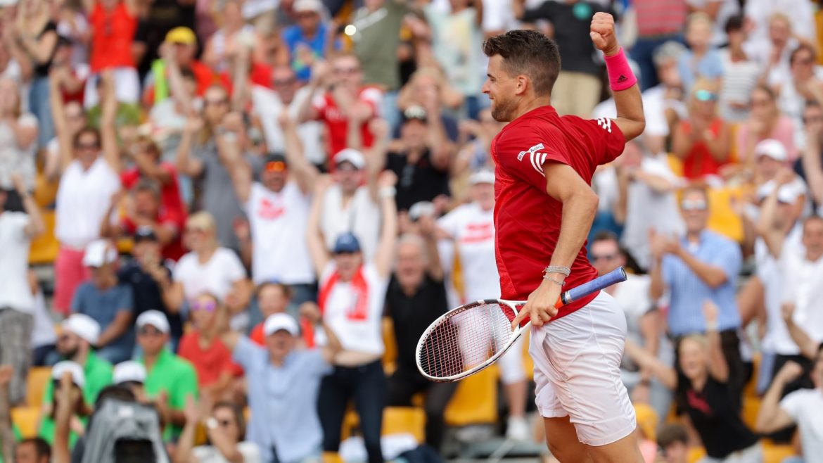 Ein Tennisspieler jubelt mit erhobener Faust, während eine jubelnde Menge in einem Stadion hinter ihm steht.