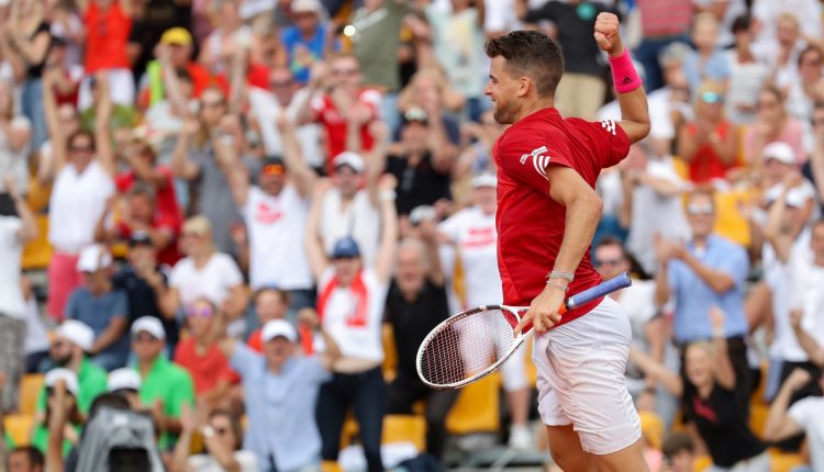 Ein Tennisspieler jubelt mit erhobener Faust, während eine jubelnde Menge in einem Stadion hinter ihm steht.