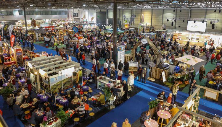 Eine geschäftige Messe oder Ausstellung mit vielen Ständen, Auslagen und Menschen, die herumlaufen, sitzen und sich unterhalten.