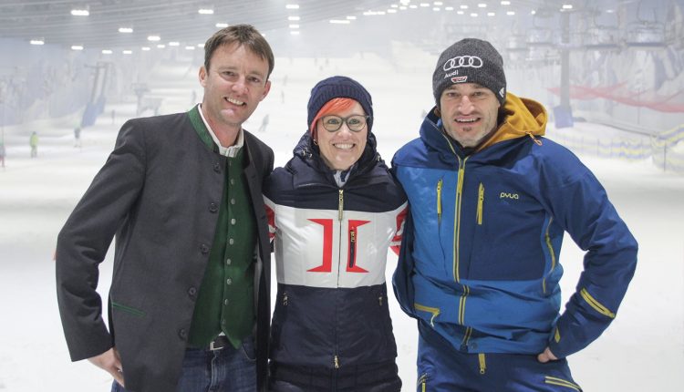 Drei Personen in Winterkleidung lächeln gemeinsam auf einer Skipiste.