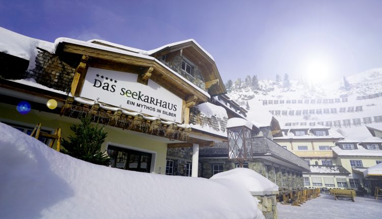 Ein verschneites Alpenhotel mit dem Schild "Das Seekarhaus" unter einem strahlend sonnigen Winterhimmel.