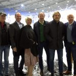 Sechs Erwachsene stehen zusammen und lächeln in einer Skihalle mit verschneitem Hintergrund.