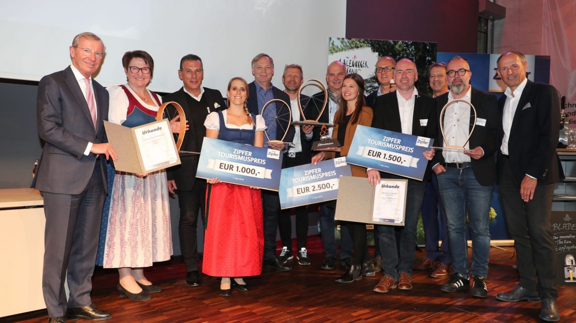 Eine Gruppe von Personen posiert mit Preisschecks und Urkunden bei einer Preisverleihung in einem Innenraum.