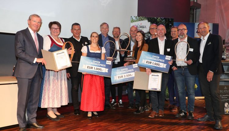 Eine Gruppe von Personen posiert mit Preisschecks und Urkunden bei einer Preisverleihung in einem Innenraum.