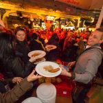 Menschen versammeln sich an einem belebten Essensstand und nehmen auf einem lebhaften Nachtmarkt im Freien Teller mit Essen entgegen.