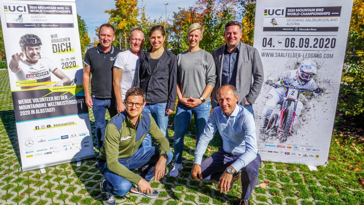 Sieben Personen posieren im Freien zwischen zwei Plakaten für die UCI Mountainbike-Weltmeisterschaften 2020 in Leogang.