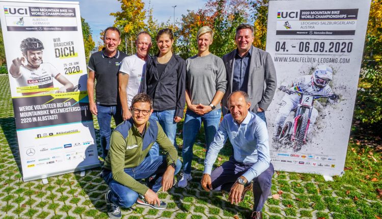 Sieben Personen posieren im Freien zwischen zwei Plakaten für die UCI Mountainbike-Weltmeisterschaften 2020 in Leogang.