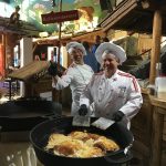 Zwei lächelnde Köche in weißen Uniformen bereiten große Pfannkuchen in einem rustikalen Restaurant zu.