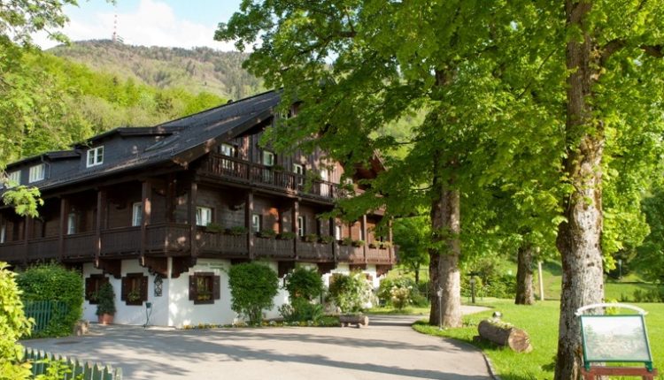Ein traditionelles Holzhaus mit Balkonen, umgeben von üppig grünen Bäumen an einem sonnigen Tag.