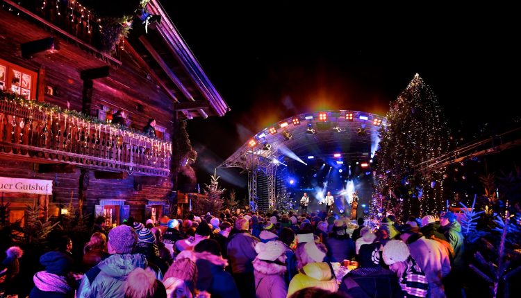 Eine festliche Menschenmenge genießt ein lebhaftes nächtliches Konzert im Freien, umgeben von Lichtern und geschmückten Gebäuden.