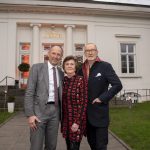 Drei Personen posieren und lächeln vor einem weißen Gebäude mit der Aufschrift Theater im Zimmer.