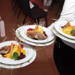 Ein Servierer hält drei Teller mit Gourmetgerichten mit Fleisch, Gemüse und bunten Beilagen.