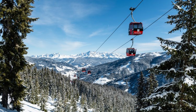 Rote Seilbahnen fahren über schneebedeckte Kiefern und Berge unter einem klaren blauen Himmel.