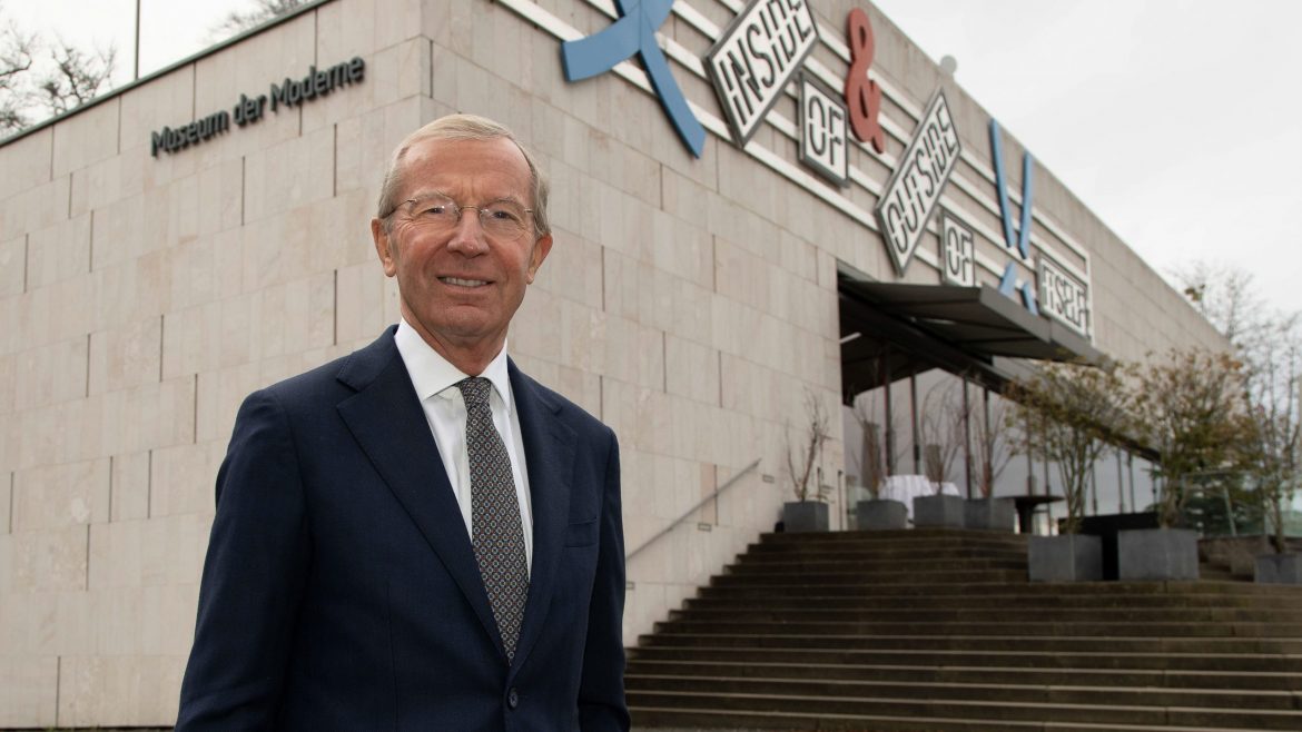 Ein lächelnder Mann im Anzug steht vor dem Gebäude des Museums der Moderne mit einer Beschilderung für moderne Kunst darüber.