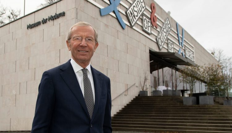 Ein lächelnder Mann im Anzug steht vor dem Gebäude des Museums der Moderne mit einer Beschilderung für moderne Kunst darüber.