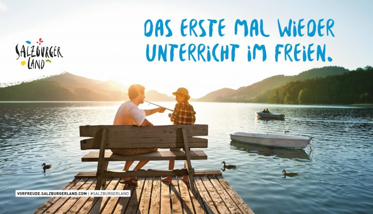 Zwei Personen sitzen auf einer Bank am Seeufer und angeln bei Sonnenuntergang mit Bergen und Wasser im Hintergrund.
