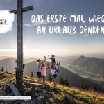 Eine Wanderfamilie gibt sich bei Sonnenuntergang in der Nähe eines großen Kreuzes auf einem Berg mit Blick auf ein malerisches Tal die Hand.