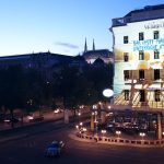 Ein Gebäude in der Abenddämmerung zeigt ein buntes projiziertes Bild mit deutschem Text an seiner Fassade, die auf eine ruhige Straße ausgerichtet ist.