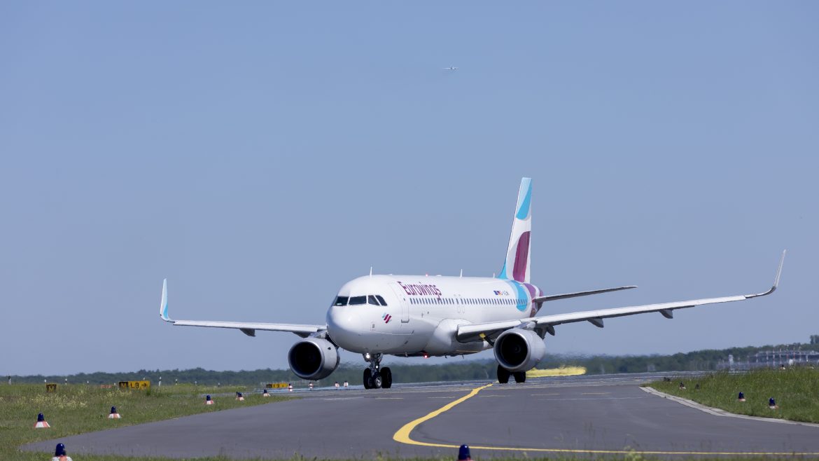 Ein weißes Passagierflugzeug rollt unter blauem Himmel auf einer Landebahn.