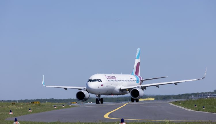 Ein weißes Passagierflugzeug rollt unter blauem Himmel auf einer Landebahn.