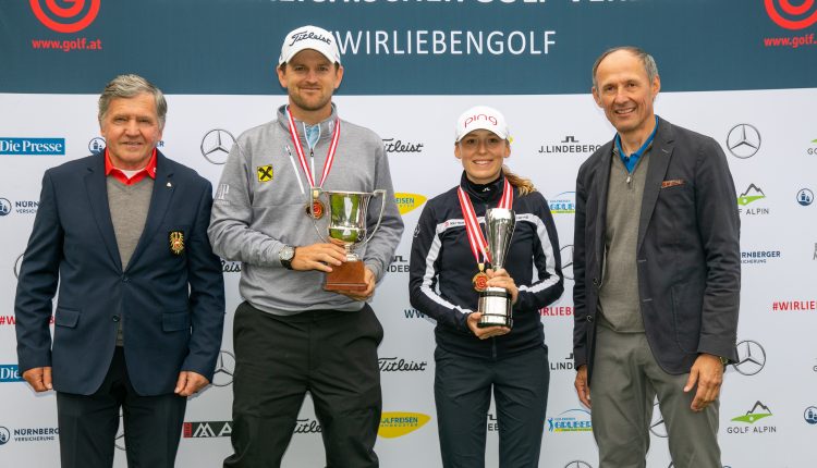 Vier Personen posieren bei einer Golfveranstaltung; zwei von ihnen halten Trophäen und Medaillen und stehen vor einem Markenhintergrund.