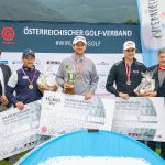 Drei Golfer posieren mit Trophäen und großen Schecks, flankiert von Offiziellen, bei einer österreichischen Golfmeisterschaft.