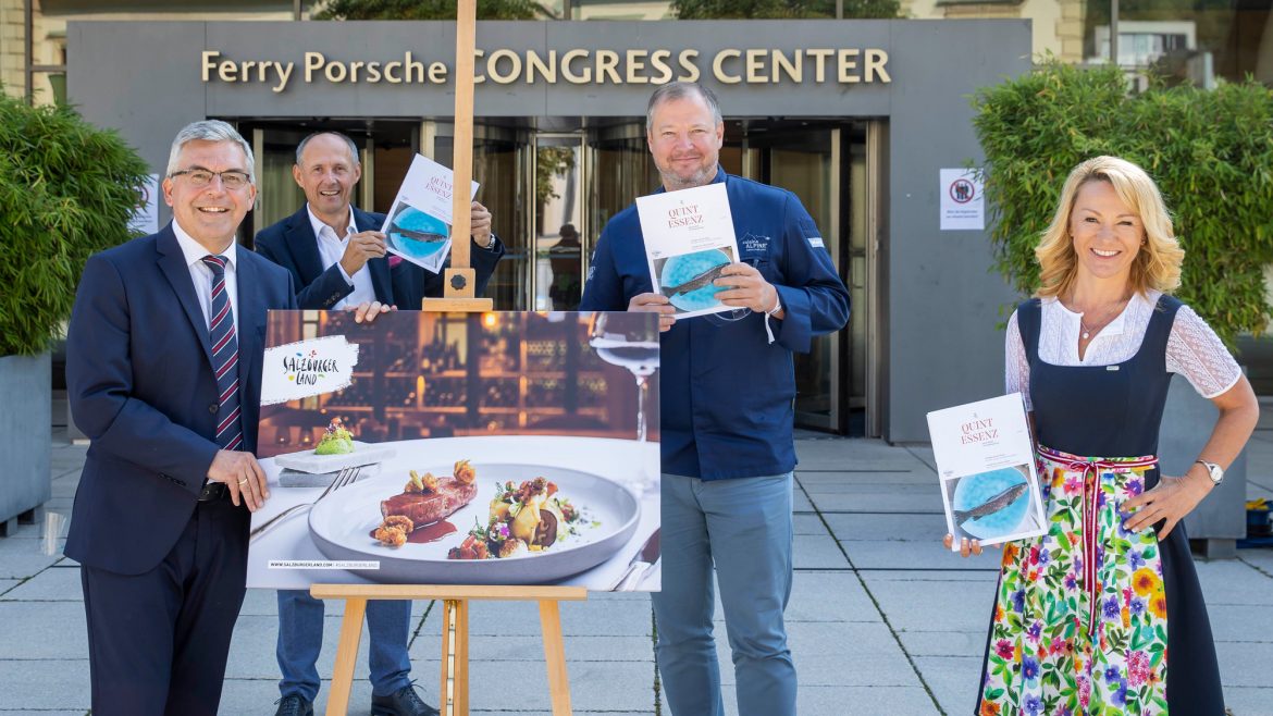 Vier lächelnde Menschen mit Büchern in der Hand stehen neben einem Foto mit Lebensmitteln auf einer Staffelei vor einem Kongresszentrum.