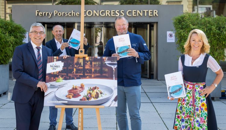 Vier lächelnde Menschen mit Büchern in der Hand stehen neben einem Foto mit Lebensmitteln auf einer Staffelei vor einem Kongresszentrum.