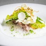 Ein Gourmet-Gericht mit Grünzeug, Schaum, dünn geschnittenem Gemüse und Beilagen auf einem weißen Teller.