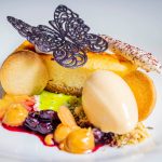 Ein Dessert auf einer Platte mit Käsekuchen, Eis, Fruchtsauce, Keksen und einem dekorativen Schokoladenschmetterling.