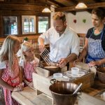 Eine Familie in Schürzen versammelt sich um einen Tisch und stellt in einer rustikalen Küche gemeinsam Käse her.