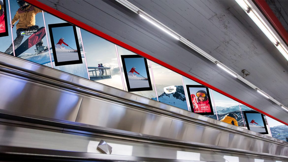 An der Wand über einer Rolltreppe in einer U-Bahn oder einem Bahnhof hängt Werbung für Skifahren und Snowboarden.