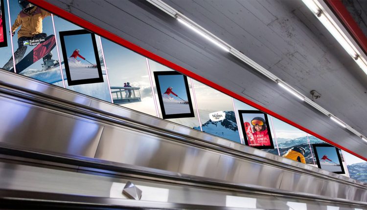 An der Wand über einer Rolltreppe in einer U-Bahn oder einem Bahnhof hängt Werbung für Skifahren und Snowboarden.
