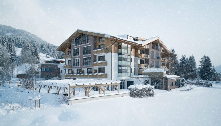Ein großes österreichisches Hotel im Chalet-Stil, umgeben von schneebedeckten Bäumen und Bergen bei Schneefall.