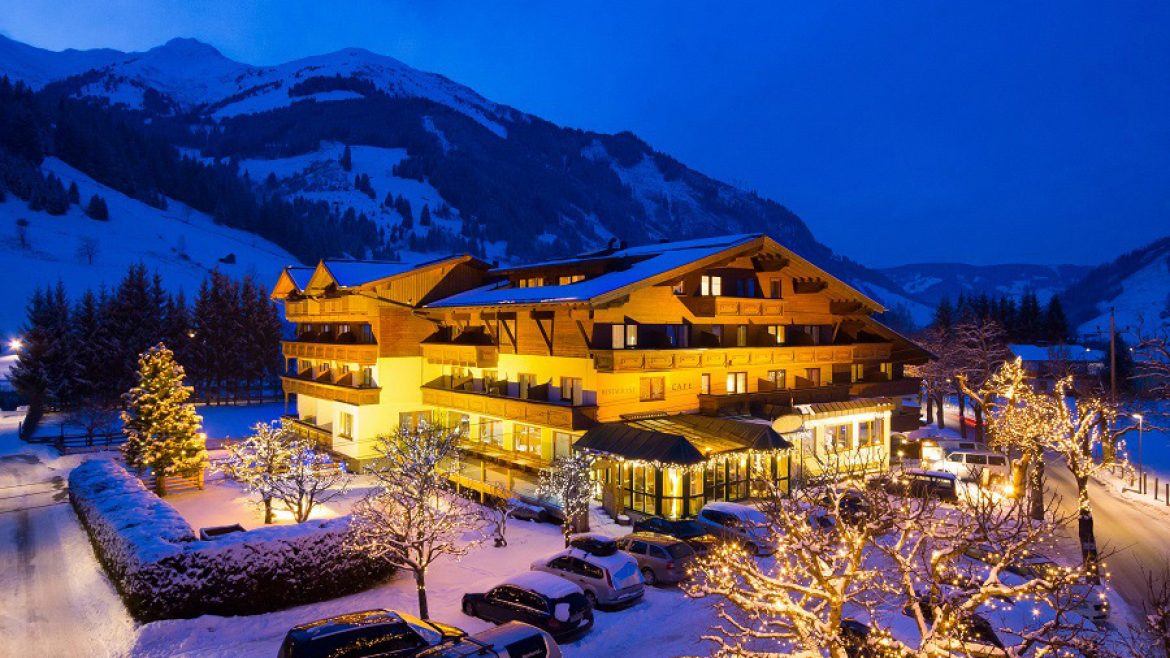 Ein hell erleuchtetes Berghotel, umgeben von Schnee und geschmückten Bäumen an einem Winterabend.