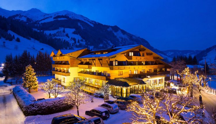 Ein hell erleuchtetes Berghotel, umgeben von Schnee und geschmückten Bäumen an einem Winterabend.