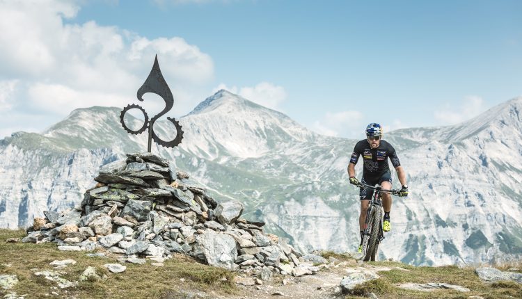 Ein Radfahrer fährt mit seinem Mountainbike auf einem felsigen Weg in der Nähe eines Steinhaufens mit Bergen im Hintergrund.