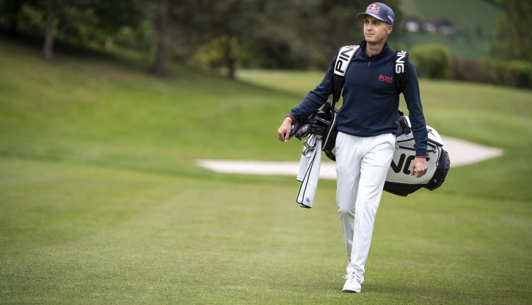 Ein Golfer mit einer Mütze geht auf einem Golfplatz und trägt eine Golftasche über der Schulter.