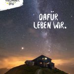 Eine Berghütte unter einem sternenklaren Nachthimmel mit Milchstraße, der Text lautet Dafür leben wir.
