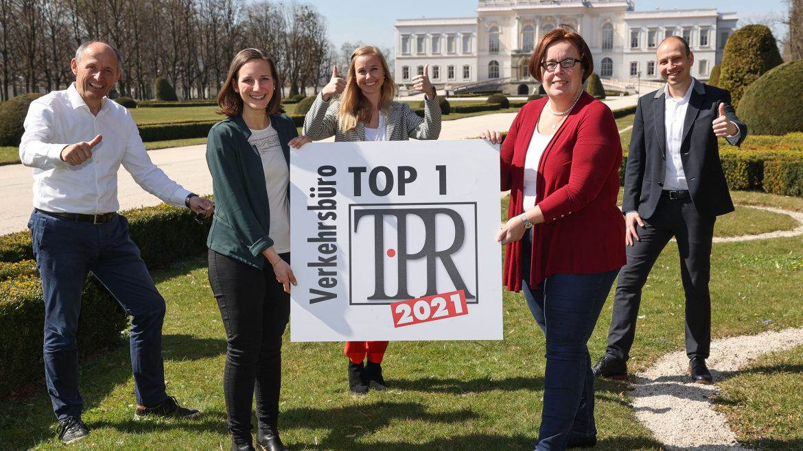 Fünf lächelnde Menschen im Freien, die ein Schild mit der Aufschrift TOP 1 Verkehrsbüro TPR 2021 halten und Daumen hoch zeigen.