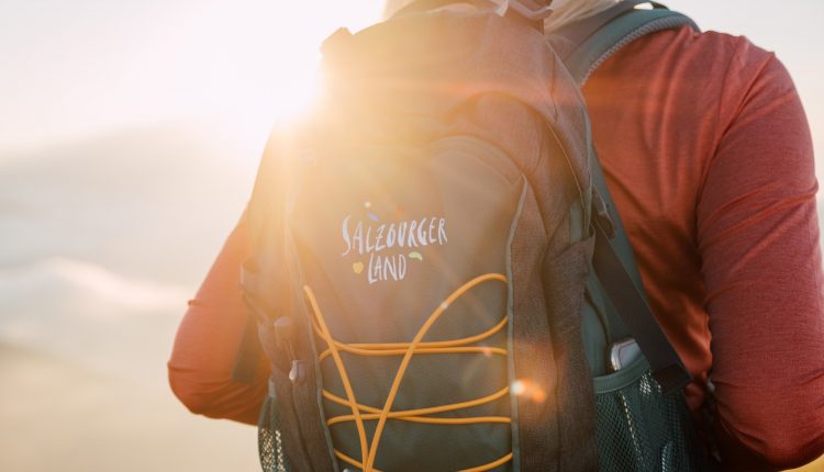 Person mit einem Salzburger Land-Rucksack im Freien, im Hintergrund scheint das Sonnenlicht.