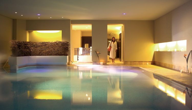 Eine Frau in einem weißen Bademantel betritt einen Indoor-Spa-Pool mit warmer Beleuchtung und modernem Dekor.